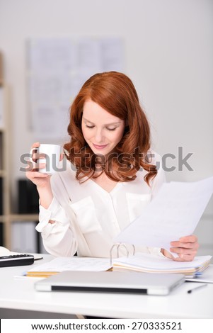 Close up Busy Young Pretty Office Woman Reading Documents While Holding a Cup of Coffee at her Office.