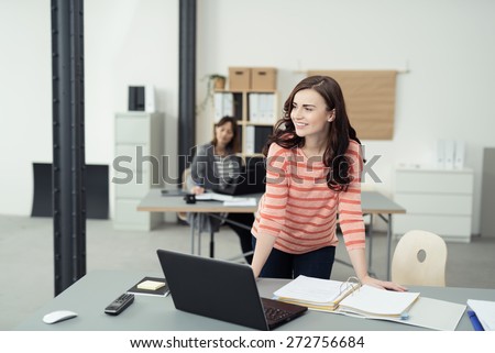 Smiling Pretty Young Office Woman Leaning on the Table Inside the Office with Laptop, Phone and Documents While Looking Afar