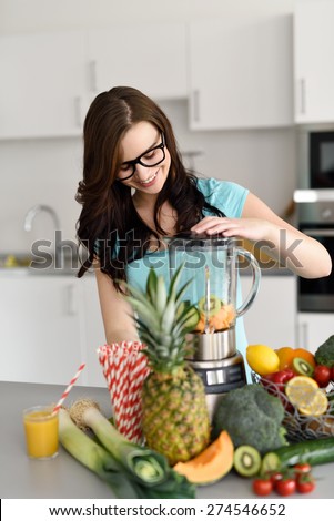 Smiling Young Woman Wearing Eyeglasses Making Health Shake in Blender Using Wide Variety of Fruits and Vegetables