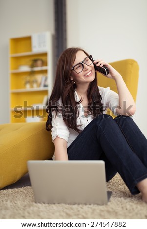 Happy Pretty Girl with Long Brown Hair Talking to Someone on Mobile Phone with Laptop on Side While Sitting on the Floor