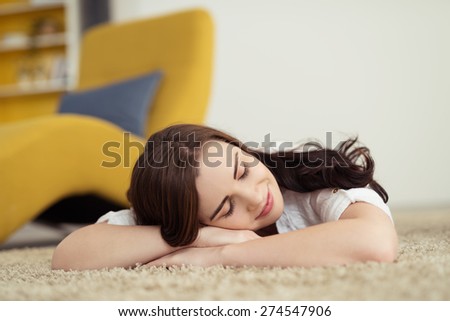 Pretty young woman relaxing on the carpet lying on her stomach with her head on her folded arms with her eyes closed and a smile of pleasure