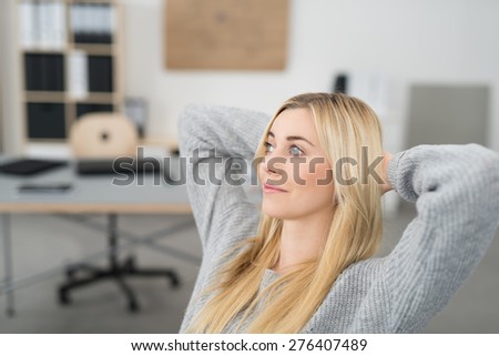 Young woman sitting thinking in the office relaxing in her chair with her hands behind her neck staring off into the air with a contemplative expression