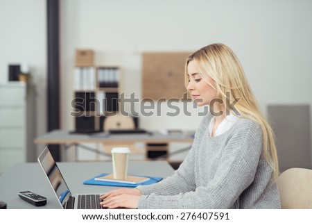 Serious Young Blond Woman Typing Something on her Laptop Computer at her Table Inside the Office.