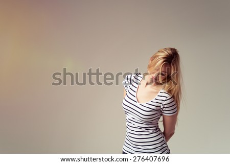 Young Blond Woman Wearing Striped T-Shirt with Hands Behind Back and Leaning to the Side in Studio with Copy Space as seen from Waist Up