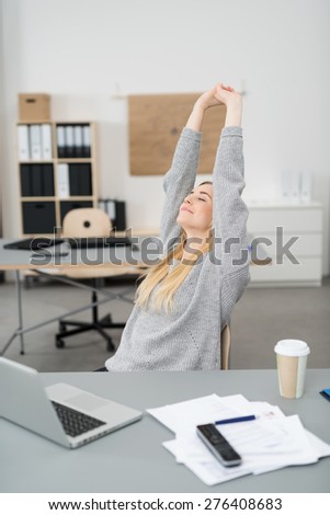 Young businesswoman stretching at her desk in the office with a smile of pleasure as she finishes her work