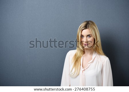 Portrait of Young Blond Woman Wearing Light Colored Blouse Standing Against Blue Grey Background Looking Confident at Camera