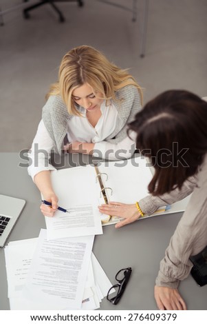 Two businesswomen discussing paperwork at a desk as they check and analyse a printed report together, high angle view