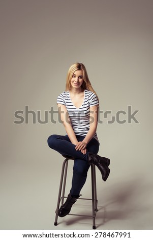 Portrait of a Stylish Pretty Girl in Trendy Attire Sitting on a Bar Stool with Legs Crossed on a Brown Background.