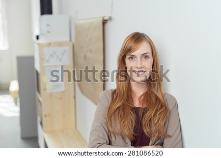 Smiling attractive redhead office worker leaning against a wall looking at the camera with a warm friendly smile