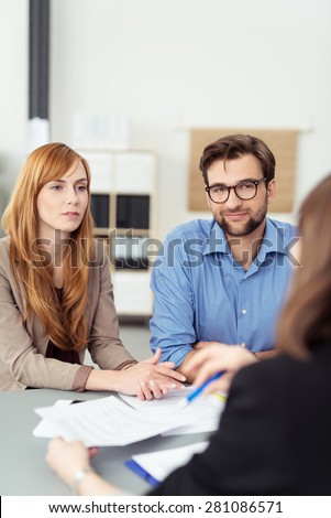 Young couple meeting with a broker or agent sitting at her desk in the office listening to te presentation with attentive expressions
