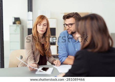 Young couple meeting with their investment broker discussing a document with her during the presentation, view over the agents shoulder