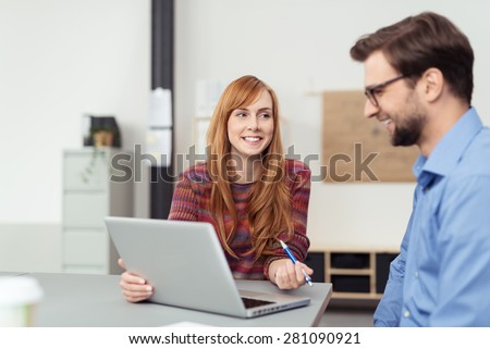 Happy young business team of a smiling friendly man and woman sitting together at a desk working on a laptop