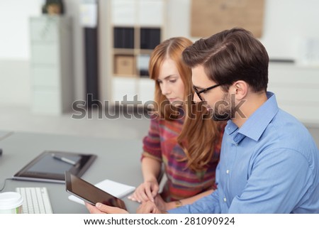 Businessman discussing a report on a tablet computer with a female colleague as they sit side by side reading the screen