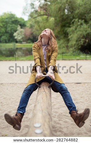 Happy Blond Teen Girl, Wearing Trendy Outfit, Enjoying her Past Time on Wooden Seesaw at the Park