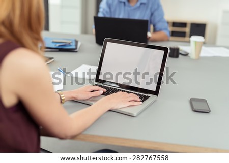 Modern business office where employees, man and woman, work on laptops and keep documents, files and mobile phones on the same shared desk