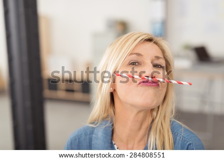 Playful middle-aged blond woman having fun balancing a straw on her upper lip while looking at the camera
