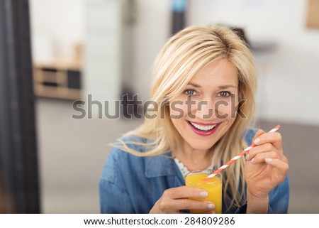 Healthy happy attractive middle-aged blond woman drinking fresh orange juice looking at the camera with a beaming smile