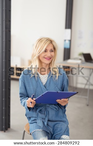 Friendly smiling middle aged woman waiting to take notes at a meeting sitting with a clipboard and pen in her hands indoors in an office