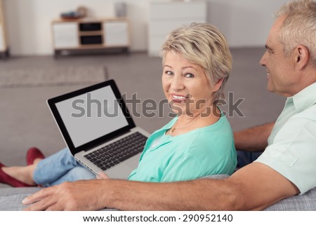 Happy Middle Aged Wife with Laptop Computer, Sitting on the Couch Next to her Husband and Smiling at the Camera.