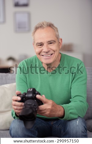 Portrait of a Happy Middle Aged Guy Sitting on the Couch, Holding his DSLR Camera While Looking at the Camera.