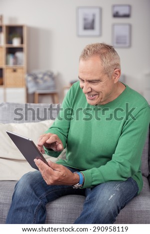 Happy Middle Aged Man in Casual Wear, Sitting at the Couch in the Living Room While Using his Tablet Computer.