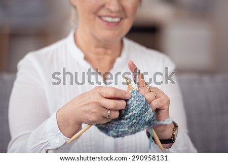 Middle-aged woman knitting a garment on plastic knitting needles with a closeup view of her hands and the needlework