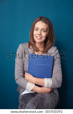 Portrait of a Pretty Office Woman Sitting on a Stool and Holding Documents Folder, Smiling at the Camera Against Blue Green Wall Background.