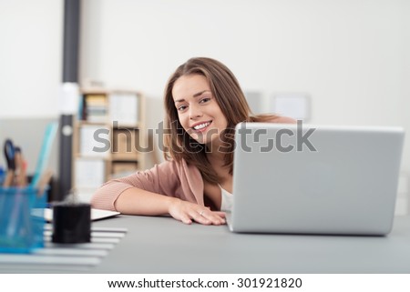 Cheerful Young Office Woman Sitting at her Desk, Smiling at the Camera Behind her Laptop Computer.