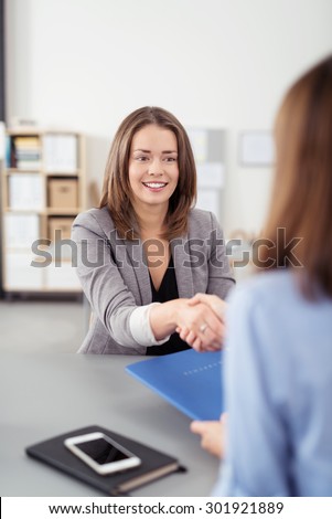 Attractive Young Female Business Agent Shaking Hands with the Client While Sitting at the Table Inside the Office.