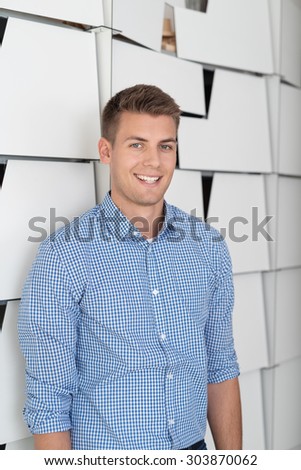 Half Body Shot of a Happy Good Looking Businessman Leaning his Back Against White File Cabinets inside the Office and Smiling at the Camera.
