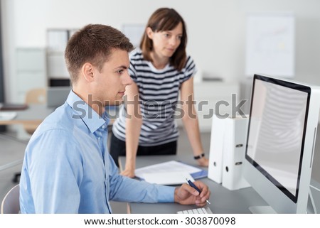 Two Young Office Workers Looking at Something on the Computer Screen on Top of the Table Together