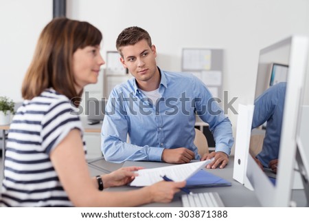 Two Office Workers Sitting at the Table Inside the Office and Looking at the Computer Screen Together to Verify Some Information.