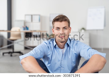 Handsome Young Office Man Sitting on the Floor with Arms on Knees and Staring Straight at the Camera.