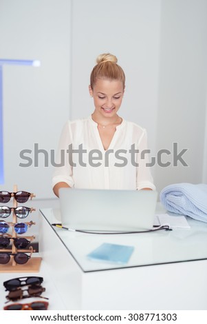 Pretty Smiling Young Woman Using a Laptop Computer on a Table Inside a Retail Fashion Store