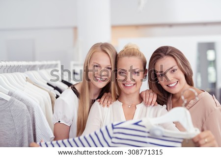 Three Pretty Young Girl Friends Smiling at the Camera While Shopping for Clothes Inside a Clothing Store.