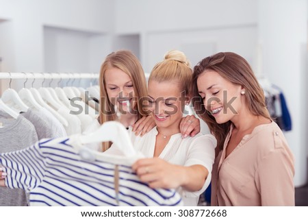 Three Young Female Friends Looking at the Quality of a Shirt with Happy Facial Expressions Inside a Clothing Store.