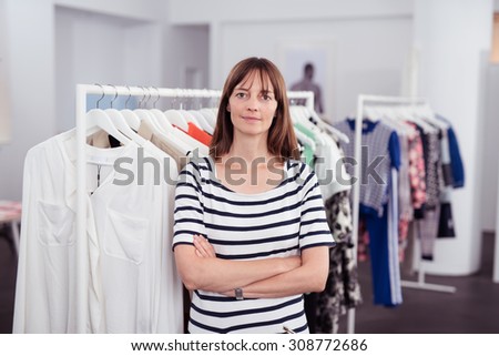 Female Owner of a Clothing Store Inside her Shop, Smiling at the Camera with Arms Crossing Over her Stomach.