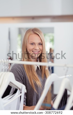 Close up Pretty Blond Young Woman Standing Behind Clothes Rail Inside a Clothing Store and Smiling at the Camera
