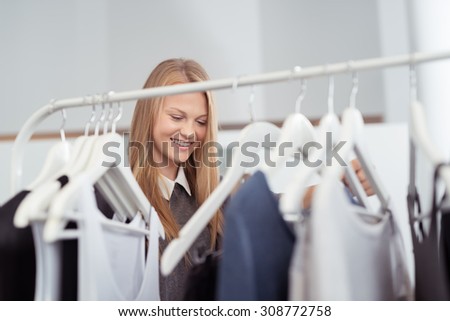 Happy Blond Woman behind Clothes Rail, Looking for Trendy Clothes Inside a Clothing Shop