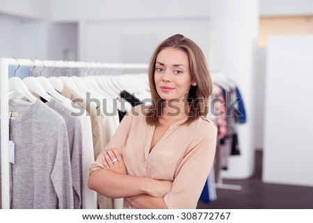 Half Body Shot of a Confident Pretty Young Woman inside a Clothing Store, Smiling at the Camera with Arms Crossing Over her Stomach.