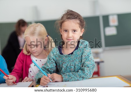 Two little girls in kindergarten class at school working side by side at a desk drawing with colored pencils on sheets of paper