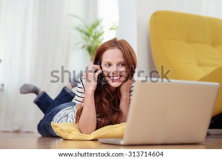 Attractive Young Woman Talking to Someone on Mobile Phone While Relaxing at the Living Room with Laptop Computer