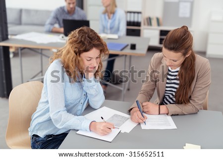 Two Young Office Women Making Some Notes Out of the Given Document at the Table Inside the Office.