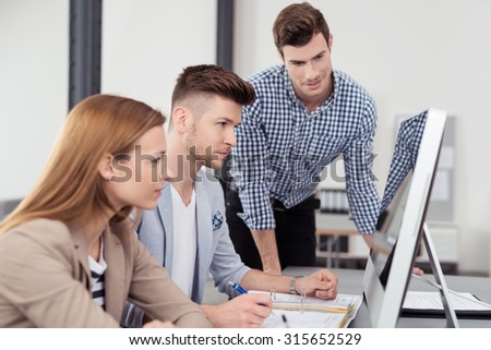 Three Young Businessmen Sitting at the Table and Looking at the Computer Screen Together with Serious Facial Expressions