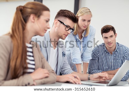 Four Young Businessmen Looking at the Laptop Screen Together While Having a Meeting Inside the Boardroom.