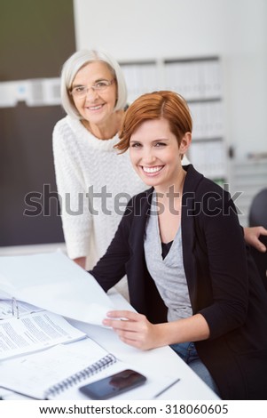 Senior and Young Businesswomen at the Table with Documents Inside the Office, Smiling at the Camera.