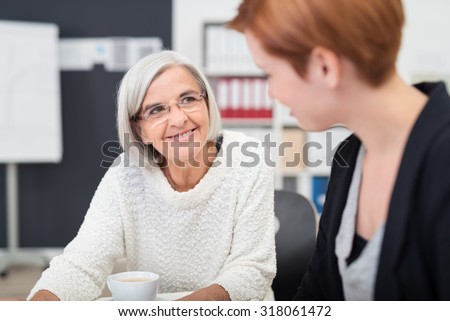 Gray Haired Senior Businesswoman with Happy Facial Expression Looking at her Colleague Inside the Office.