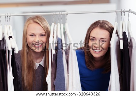 Close up Pretty Girls Smiling at the Camera Through Clothes Rail Inside the Clothing Store.