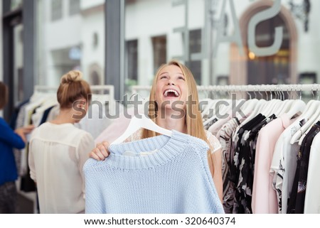 Happy Young Woman Laughing Out Loud While Holding a Hanged Shirt Inside the Clothing Store.
