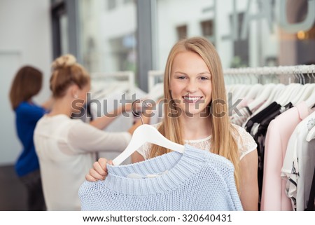 Close up Pretty Blond Girl Holding a Hanged Shirt Inside a Clothing Store and Smiling at the Camera